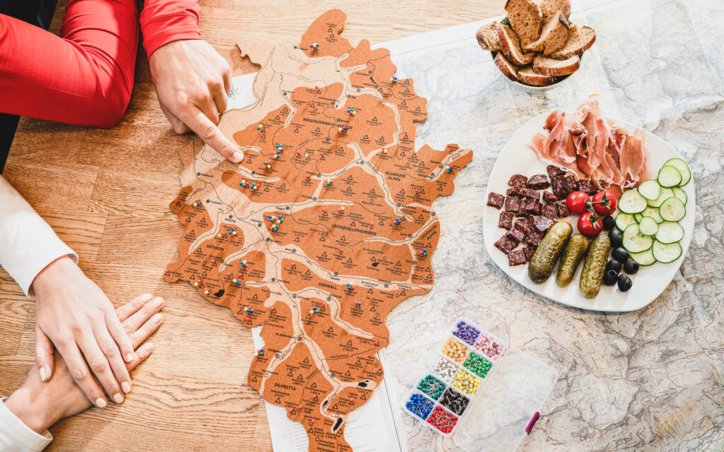 Der Alpenspinner liegt auf dem Tisch und zwei Personen pinnen mit Stecknadeln ihre gemachten Gipfel