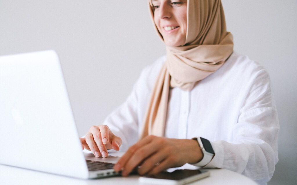 Junge Frau mit Kopftuch schreibt etwas am Laptop