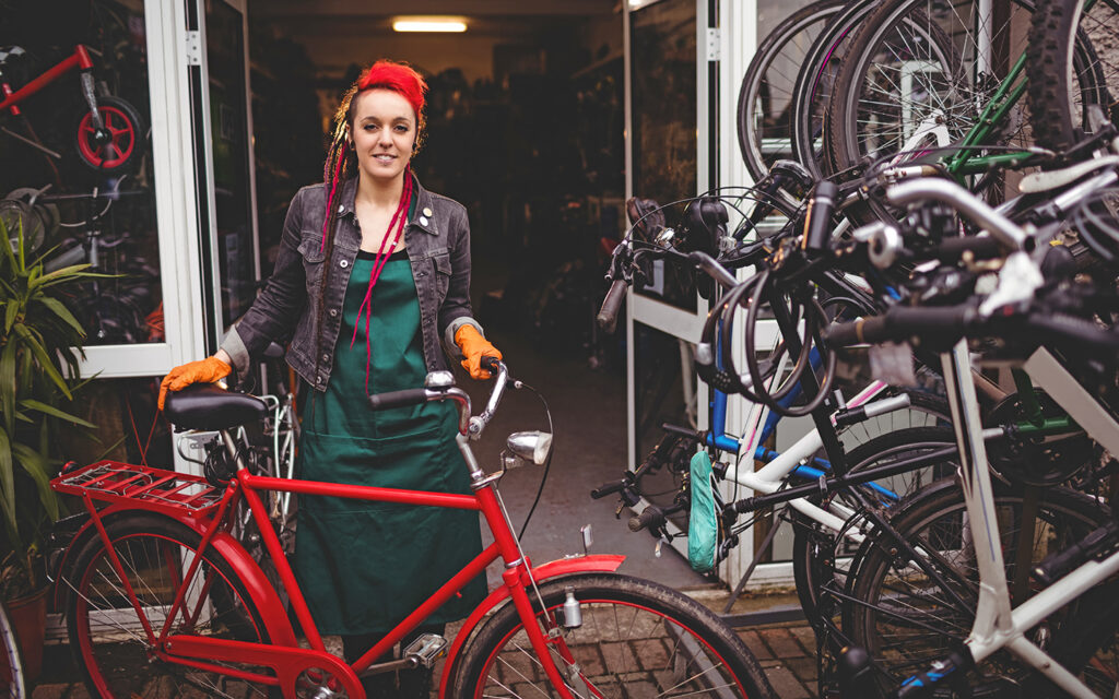 Junge Frau steht vor einem Fahrradgesch&auml;ft und zeigt ein Fahrrad