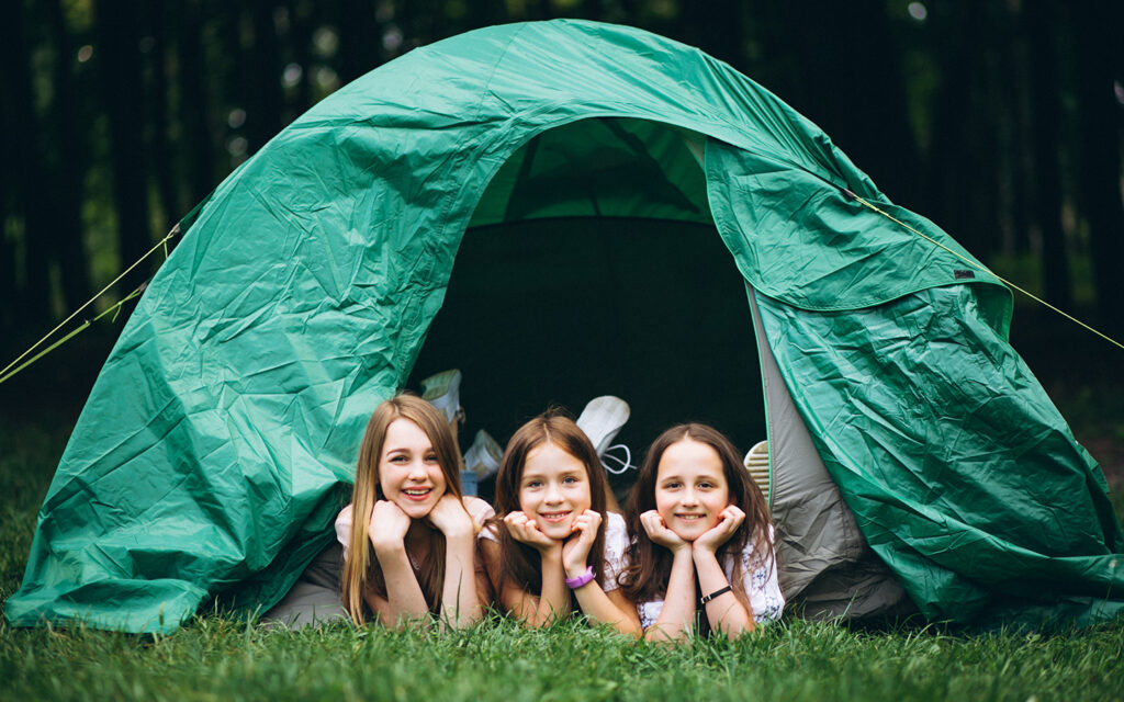 Drei Kinder schauen aus einem Zelt heraus