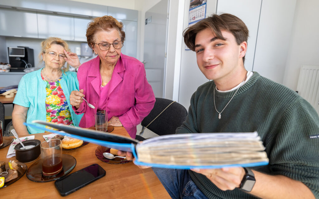 Junger Mann sitzt am Tisch mit zwei alten Menschen und schaut in eine Mappe