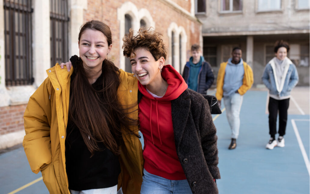 Zwei junge Frauen laufen lachend vor einer Gruppe Burschen.