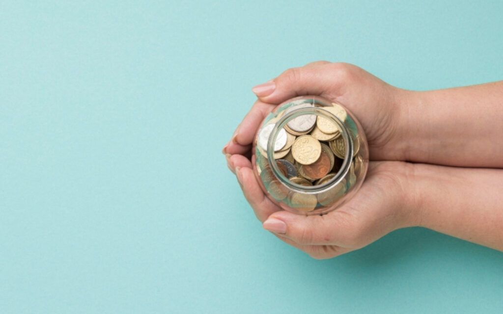 Zwei Hände halten ein Glas mit Münzen.