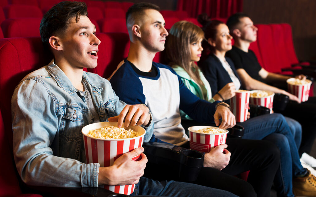 f&uuml;nf Jugendliche sitzen im Kinosaal und essen Popcorn