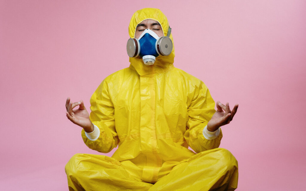 Ein Mann in einem gelben Schutzanzug und mit Maske meditiert.