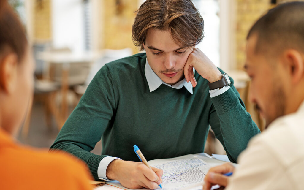 Junge sitzt mit anderen Sch&uuml;lern am Tisch und lernt