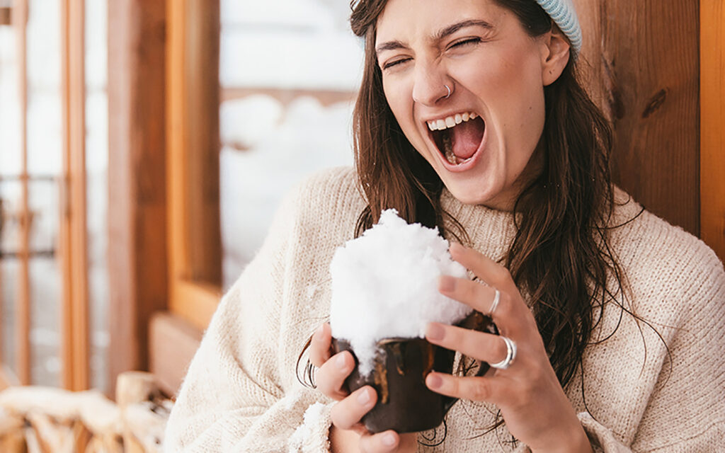 Junge Frau trinkt aus einer Tasse, die mit Schnee gef&uuml;llt ist