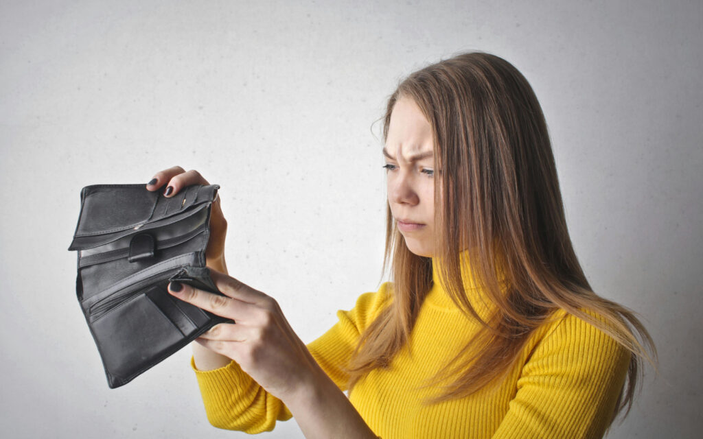 Eine junge Frau schaut verärgert in ihre leere Geldtasche.
