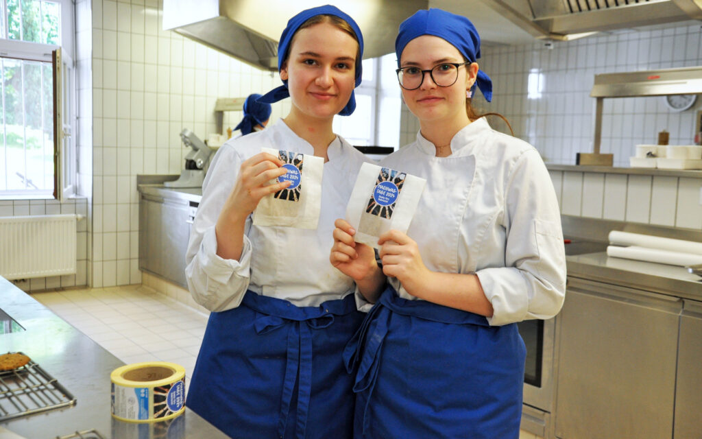 Zwei Jugendliche in Kochuniform halten Säckchen mit Keksen hoch, die sie für die MACHWAS-Tage gemacht haben.