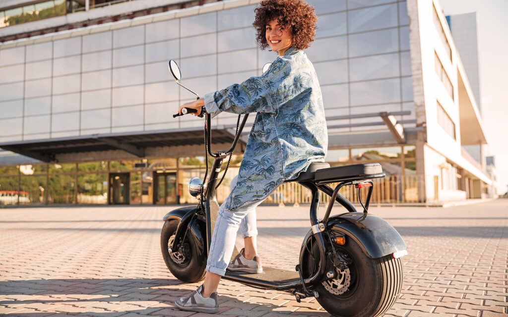 Junge Frau sitzt auf einem E-Roller und schaut in die Kamera