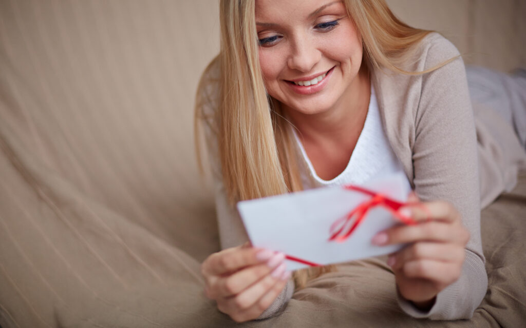M&auml;dchen liegt auf dem Sofa und &ouml;ffnet voller Freude einen Gutschein