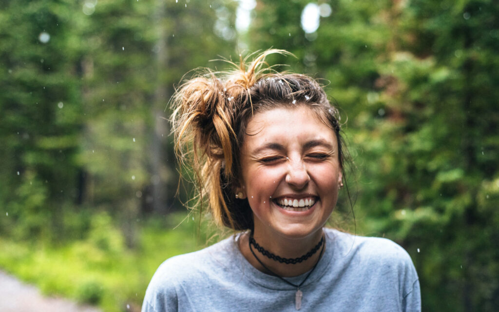 Eine Frau steht in der Natur und lacht herzhaft.