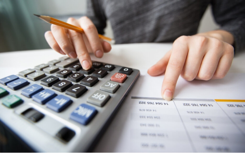 Nahaufnahme eines Buchhalters, der auf einem Taschenrechner rechnet und mit einer Tabelle arbeitet