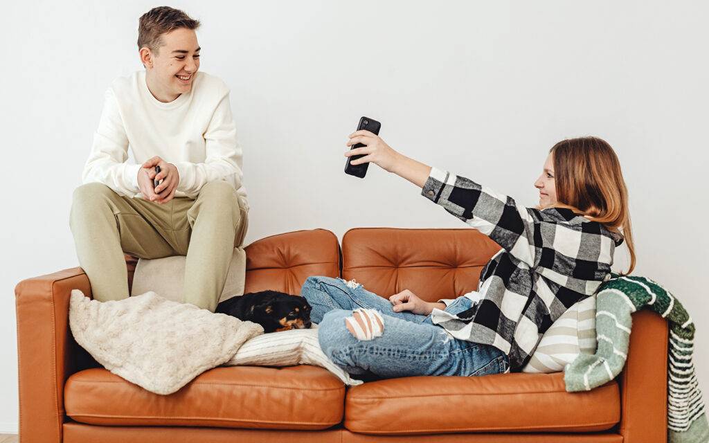 Ein Junge und ein Mädchen sitzen auf dem Sofa und das Mädchen zeigt dem Jungen etwas auf ihrem Smartphone
