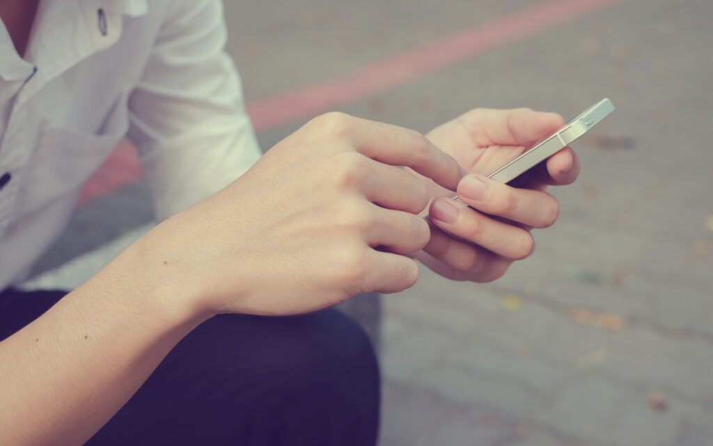 Eine Person im weißen Hemd sitzt und hält ein Smartphone in der Hand.