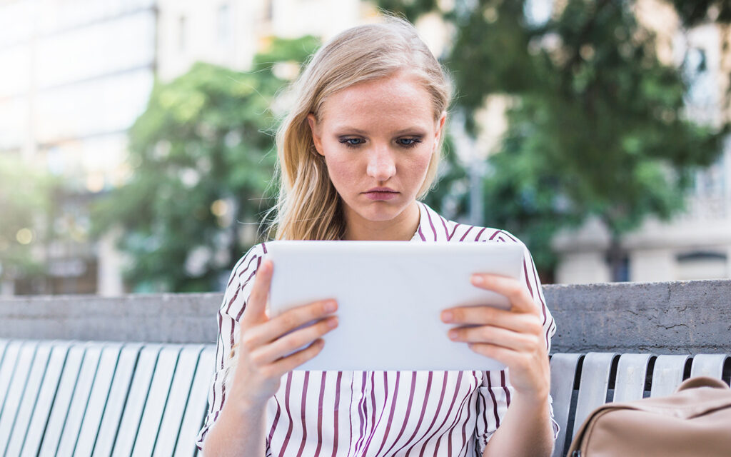 Junge Frau schaut etwas zweifelnd auf den Bildschirm eines Tablets