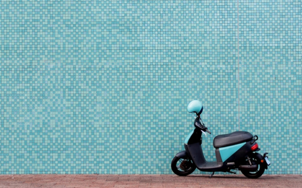 Eine Vespa steht vor einer türkis gekachelten Wand.