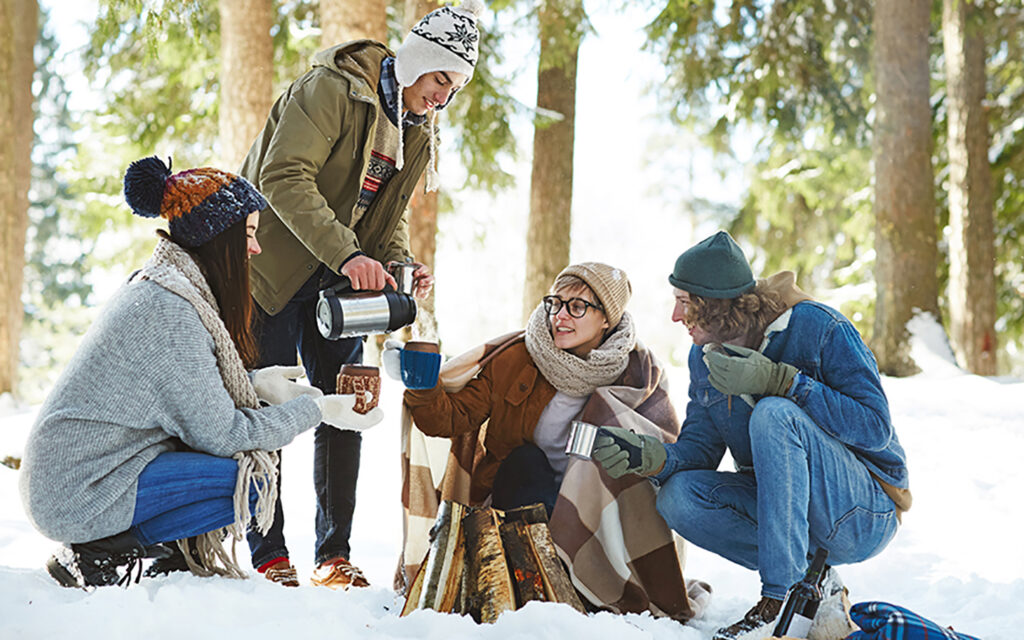 vier junge Menschen veranstalten im Freien in verschneiter Landschaft ein Winterpicknick