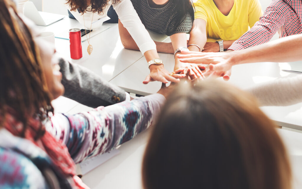 Eine Gruppe von Leuten streckt die Hände zusammen und macht eine Geste, dass sie es zusammen schaffen