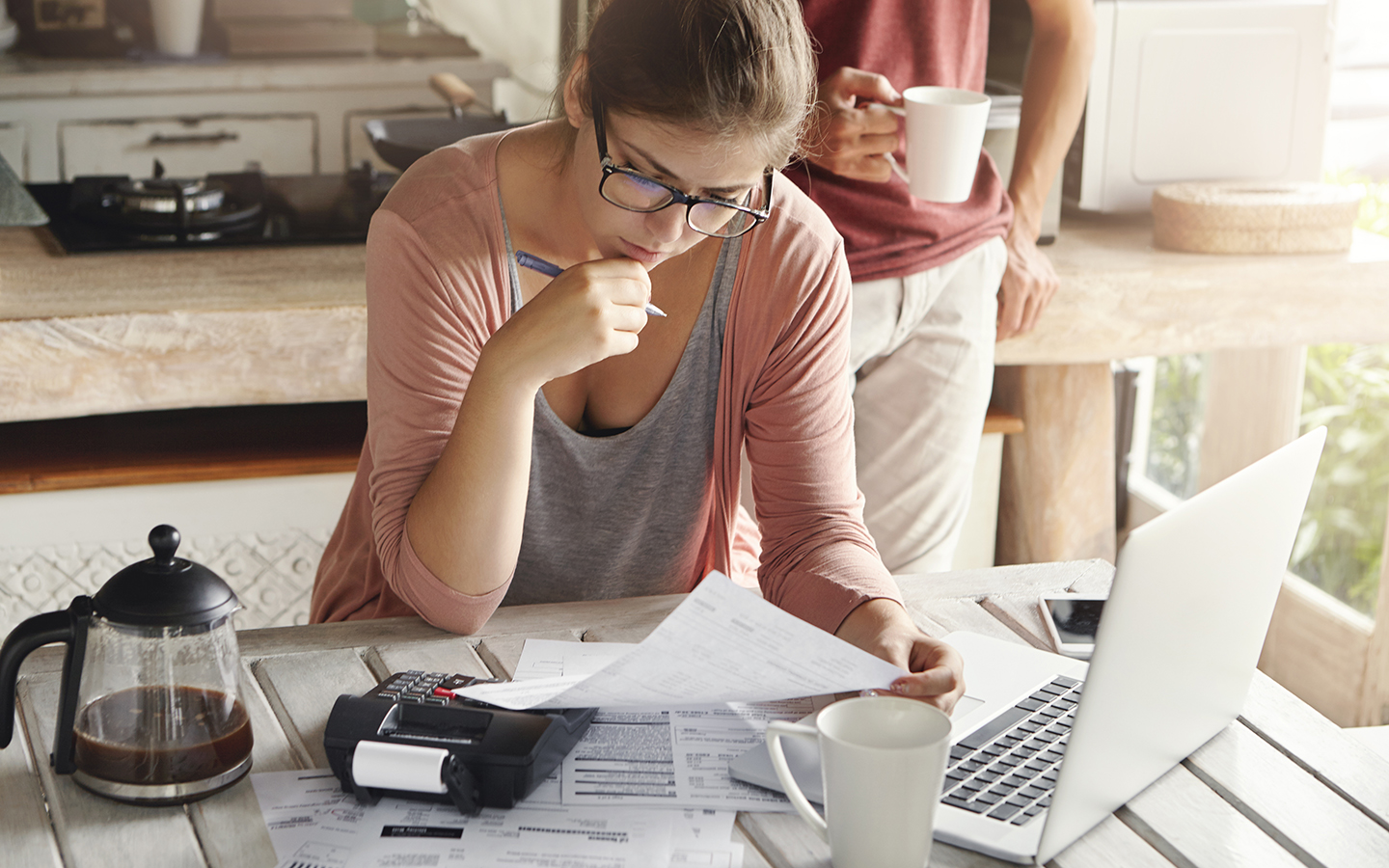 Attraktive Frau mit Brille, die ernst und konzentriert schaut, während sie mit einem Stift Formulare ausfüllt, Rechnungen berechnet, Familienausgaben kürzt und versucht, Geld zu sparen, um eine große Anschaffung zu machen.
