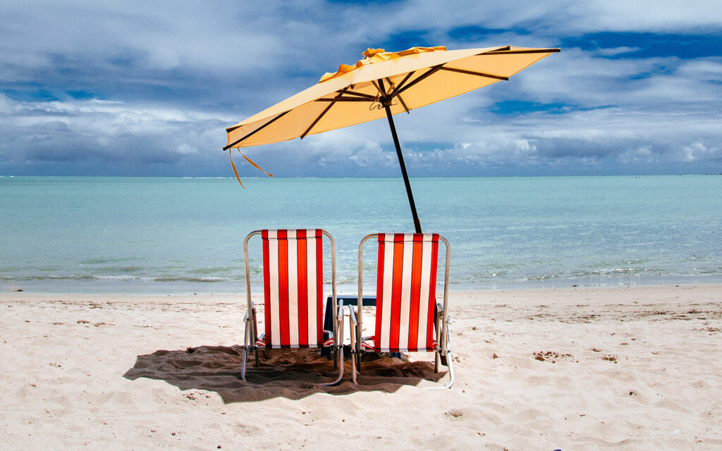 Zwei Liegestühle mit Sonnenschirm dazwischen am Meer