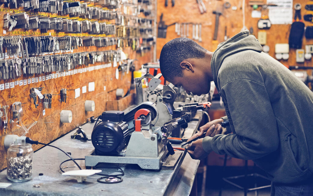 Junger Lehrling arbeitet beim Schlüsseldienst und macht Schlüssel