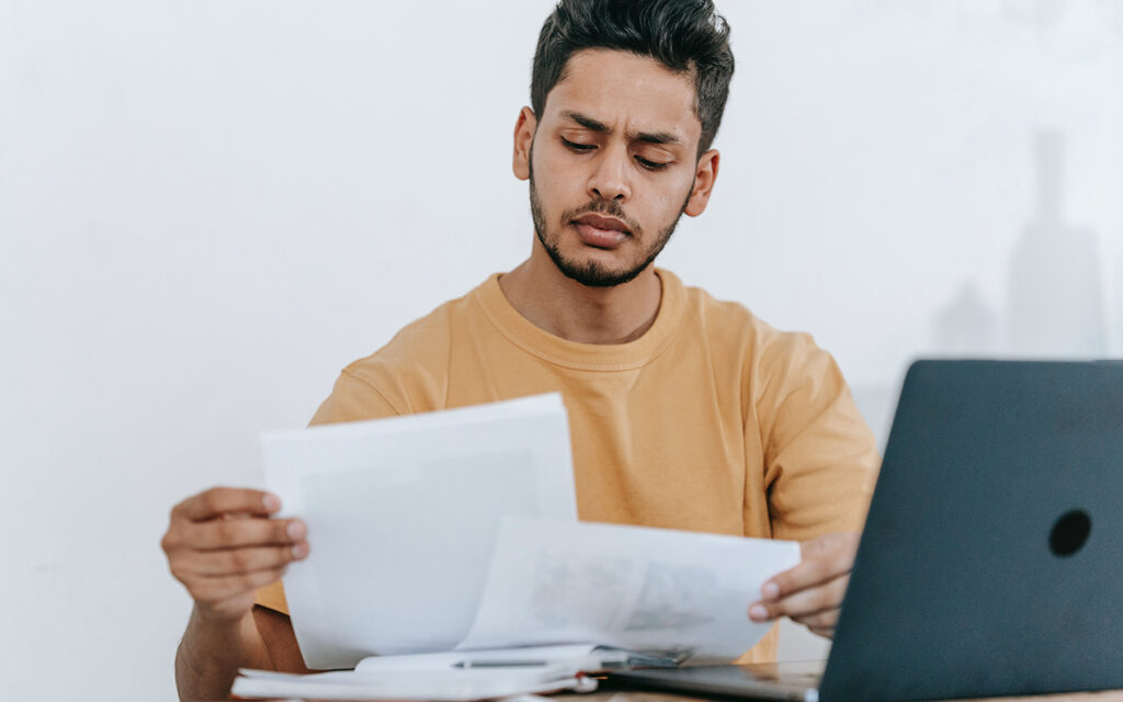 Junger Mann sieht am Schreibtisch Unterlagen durch