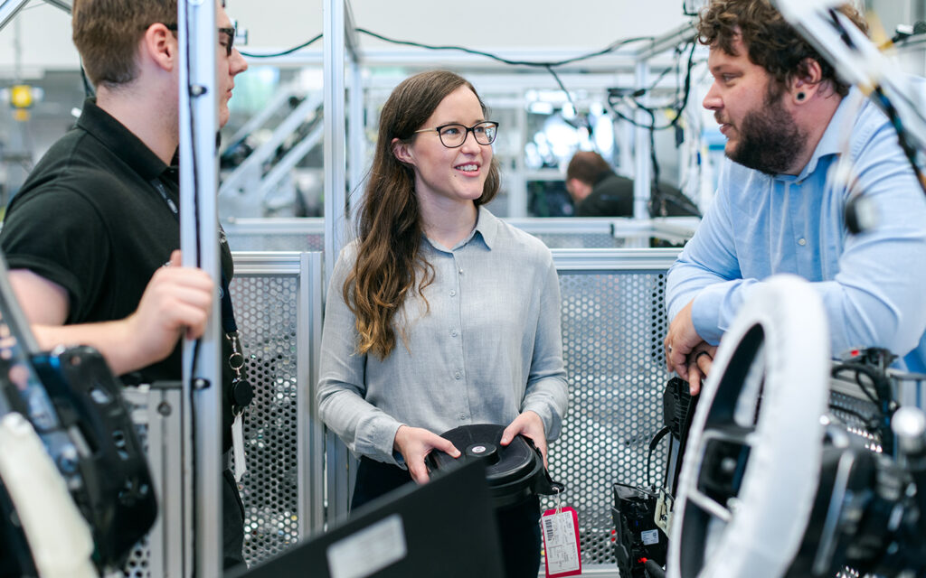 Frau arbeitet als Lehrling bei einem Automobilhersteller und spricht mit zwei Männern